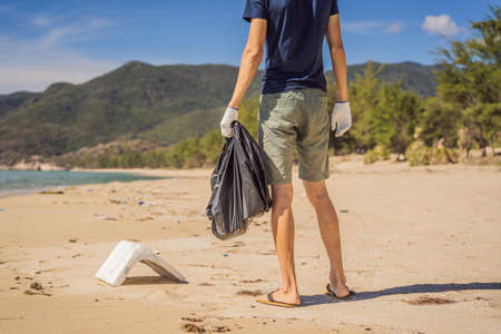 Man in gloves pick up plastic bags that pollute sea. Problem of spilled rubbish trash garbage on the beach sand caused by man-made pollution and environmental, campaign to clean volunteer in conceptの写真素材