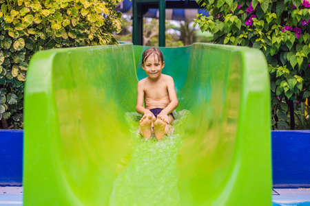 Young boy or kid has fun splashing into pool after going down water slide during summer