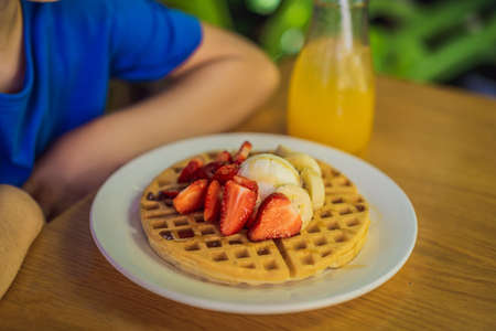 A little boy eats dessert Belgian waffles with strawberry in a cafeの写真素材