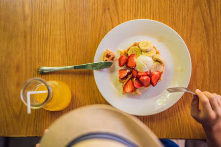 A little boy eats dessert Belgian waffles with strawberry in a cafe