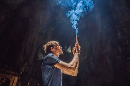 Young man praying in a Buddhist temple holding incense Huyen Khong Cave with shrines, Marble...