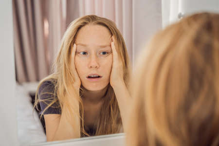 Extremly tired young woman looking at himself in the mirror, home alone. self-isolation at home, quarantine due to pandemic COVID 19. Mental health problems in self-isolation at homeの写真素材