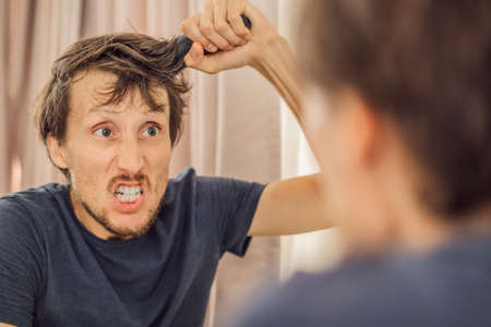 Extremly tired young man looking at himself in the mirror, home alone. self-isolation at home, quarantine due to pandemic COVID 19. Mental health problems in self-isolation at homeの写真素材