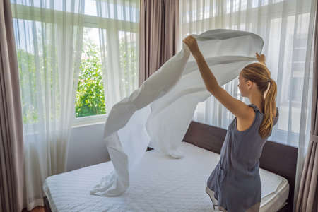 Young Female Housekeeper Changing Bedding In Hotel Room