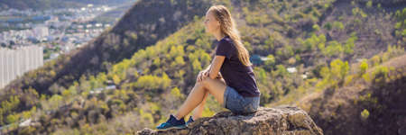 A young woman local tourist sits on a rock and enjoys the view of her city. Local tourism concept. Tourism after COVID 19 BANNER, LONG FORMATの写真素材