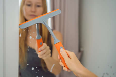 Young beautiful woman cleaning mirror. Cleaning service. Maid cleaning at home