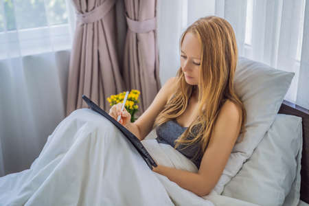 Woman draws on tablet with stylus in bed