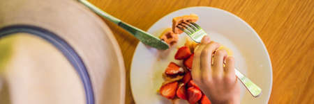 A little boy eats dessert Belgian waffles with strawberry in a cafe BANNER, LONG FORMATの写真素材