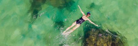 The woman is snorkeling among the corals. View from the drone BANNER, LONG FORMATの写真素材