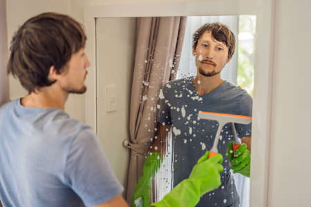 Young man cleaning mirror at home hotelの写真素材