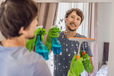 Young man cleaning mirror at home hotelの写真素材