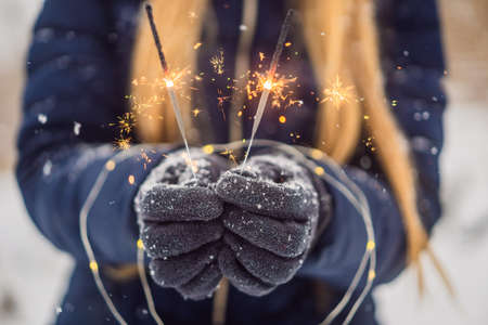 Sparklers in female hands on a background of snowfall. Christmas and New Year conceptの写真素材