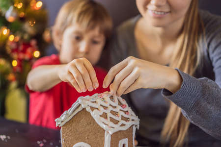 Young mother and kid making gingerbread house on Christmas eve