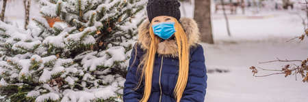Young woman enjoys a winter snowy day in a snowy forest wearing a medical mask during COVID-19 coronavirus BANNER, LONG FORMATの写真素材