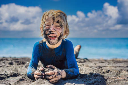 11.11 Black Friday concept. Smiling boy with dirty Black face sitting and playing on black sand...