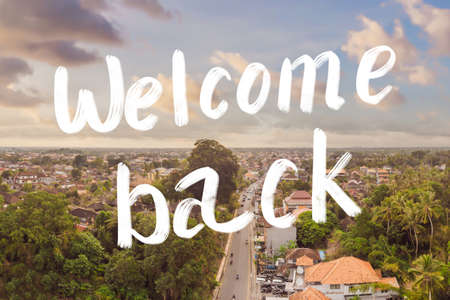 Welcome back to bali. Many villas with brown-orange shingle roofs between tropical trees on the sky background in Ubud on Bali. Sun is shining onto them. Aerial horizontal photoの写真素材