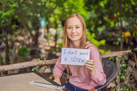 Young woman in a cafe shows a sign - I dont need a straw. No plastic. Global environmental protection issueの写真素材
