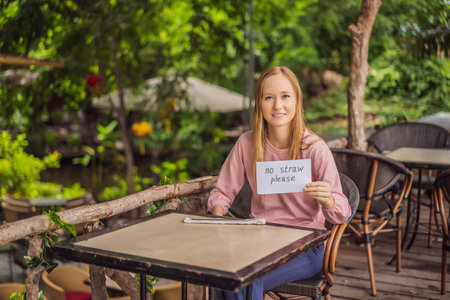 Young woman in a cafe shows a sign - no straws please. No plastic. Global environmental protection issueの写真素材