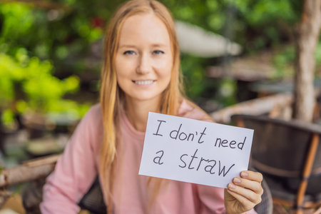 Young woman in a cafe shows a sign - I dont need a straw. No plastic. Global environmental protection issueの写真素材