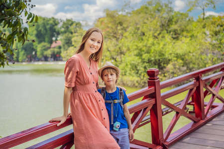 Caucasian mom and son travelers on background of Red Bridge in public park garden with trees and reflection in the middle of Hoan Kiem Lake in Downtown Hanoi. Traveling with children conceptの写真素材
