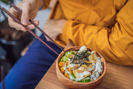 Man eating Raw Organic Poke Bowl with Rice and Veggies close-up on the table. Top view from above horizontalの写真素材