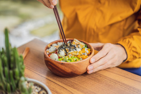 Man eating Raw Organic Poke Bowl with Rice and Veggies close-up on the table. Top view from above...