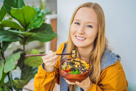Woman eating Raw Organic Poke Bowl with Rice and Veggies close-up on the table. Top view from above...