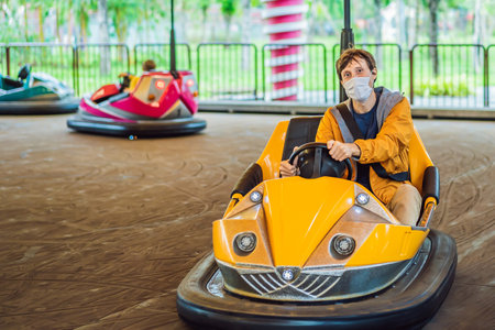 Man wearing a medical mask during COVID-19 coronavirus having a ride in the bumper car at the amusement park