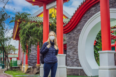 traveler in medical mask stopped on the street and looking at the Japanese, Chinese, Korean, Vietnamese traditional building. Tourists travel in Asia after the coronavirus epidemicの写真素材