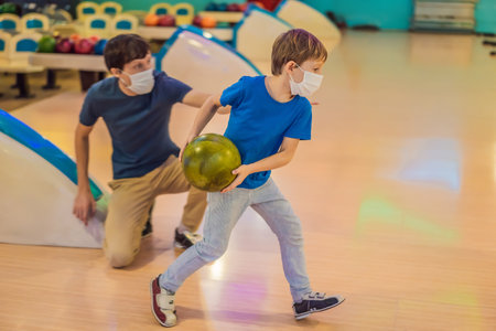 Father and son playing bowling with medical masks during COVID-19 coronavirus in bowling clubの写真素材