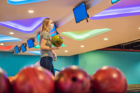 Woman playing bowling with medical masks during COVID-19 coronavirus in bowling clubの写真素材