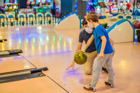 Father and son playing bowling with medical masks during COVID-19 coronavirus in bowling clubの写真素材