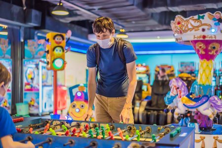 A young man wearing a medical mask during COVID-19 coronavirus playing table football indoors against a friendの写真素材
