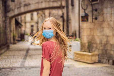 Young woman wearing a medical mask during pandemic tourist walks down the street in a European city
