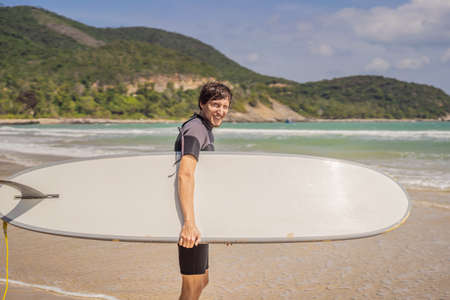 Young surfer standing agains the ocean looking the waves, professional surfer in black wetsuit...