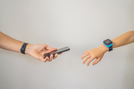 Dad's hand reaches for the hand of the child in the smart children's watch. Dad shows that his child is protected. Smart watch for baby safety. The child makes school lessons, listening to music, calling friends.の写真素材