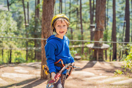Happy child in a helmet, healthy teenager school boy enjoying activity in a climbing adventure park on a summer dayの写真素材