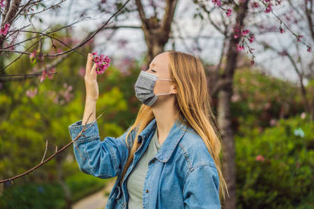 Happy woman in sakura in protective mask and smelling blooming sakura flowers after quarantineの写真素材