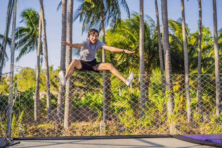 Happy man jumping on an outdoor trampoline, against the backdrop of palm treesの写真素材