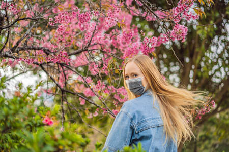Happy woman in sakura in protective mask and smelling blooming sakura flowers after  quarantine