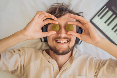 Young man, a digital artist, DJ creates digital art on a tablet at home and shows a coin with the inscription NTF - non fungible token. Remote work, digital nomad, digital painting, animation, videoの写真素材