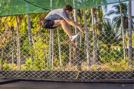 Happy man jumping on an outdoor trampoline, against the backdrop of palm treesの写真素材