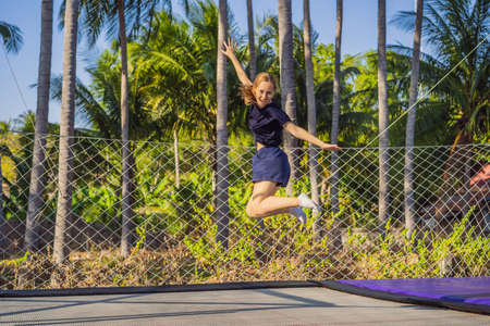 Young woman jumping on an outdoor trampoline, against the backdrop of palm trees
