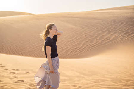 Young beautiful woman traveling in the desert. Sandy dunes and blue sky on sunny summer day. Travel, adventure, freedom concept.の写真素材