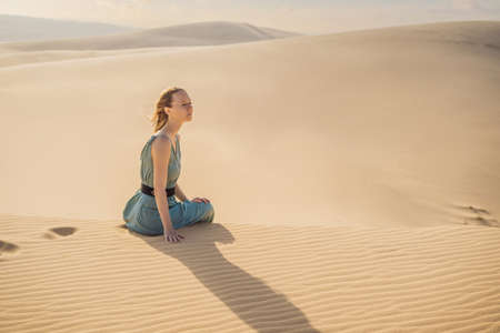 Young beautiful woman traveling in the desert. Sandy dunes and blue sky on sunny summer day. Travel, adventure, freedom concept.の写真素材