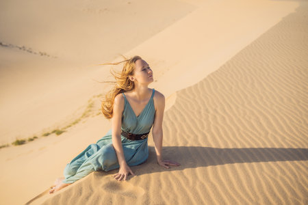 Young beautiful woman traveling in the desert. Sandy dunes and blue sky on sunny summer day. Travel, adventure, freedom concept. Tourism reopens after quarantineの写真素材