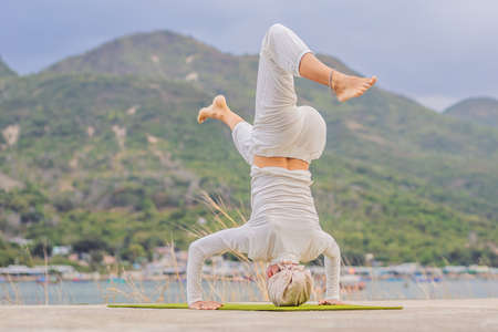 Kundalini yoga woman in white clothes and turban practices yoga kundalini on the background of the sea, mountains and sunset. Fighting face painting of the Indians shows her inner world. Visual storytelling of a woman dedicated to yoga.の写真素材