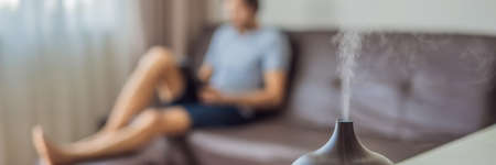 BANNER, LONG FORMAT Aromatherapy Concept. Wooden Electric Ultrasonic Essential Oil Aroma Diffuser and Humidifier. Ultrasonic aroma diffuser for home. Man resting at homeの写真素材