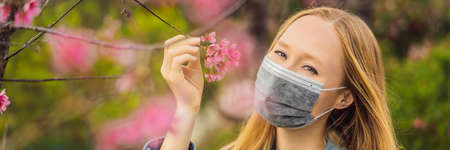 Happy woman in sakura in protective mask and smelling blooming sakura flowers