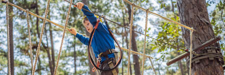 BANNER, LONG FORMAT Happy child in a helmet, healthy teenager school boy enjoying activity in a climbing adventure park on a summer dayの写真素材